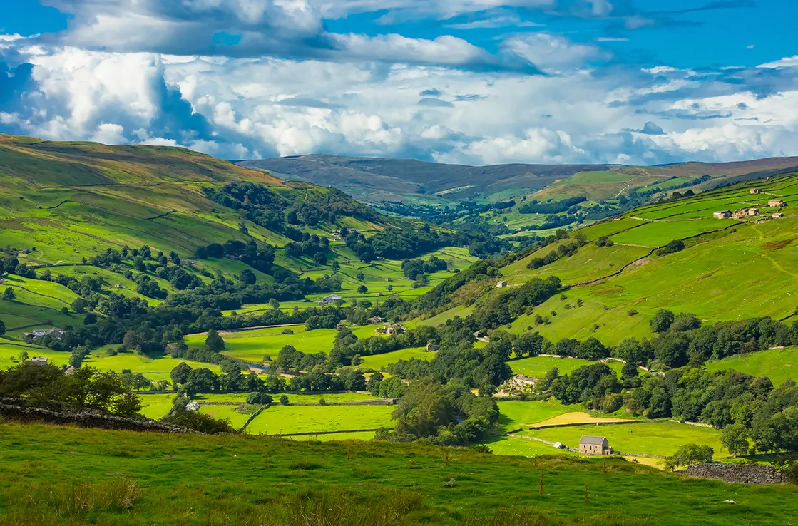 Yorkshire Dalesin laakso näyttäytyy upean vehreänä vuorten ja siintäessä taustalla poutapilvistä sinitaivasta vasten